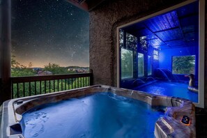 A hot tub with a starry night view, a wooden deck, and a glass enclosure with a hot tub inside.
