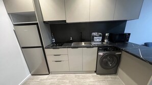 A compact kitchen with a refrigerator, microwave, sink, and washing machine.