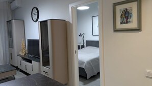 A compact hotel room with a bed, a desk, a wardrobe, and a small kitchenette.