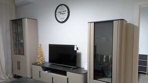 A modern living room with a flat-screen TV, a marble coffee table, a glass cabinet, and a decorative wooden structure.
