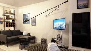 Ein modernes Hotelzimmer mit einer Couch, einem kleinen Tisch, einem Fernseher und einem Bett mit einem Streifen Teppich.