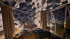 A room with a hexagonal ceiling design, a bed, curtains, and a window with a view.