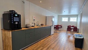 A modern kitchen with a coffee machine, a toaster, and a refrigerator. There is a dining area with red chairs and a table.