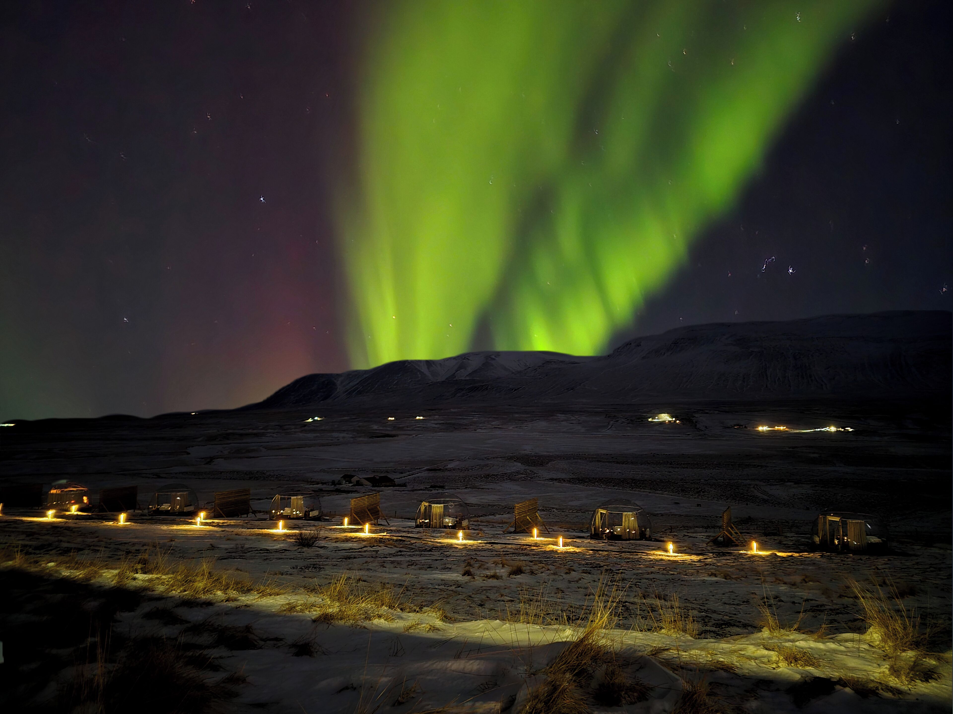 A snowy landscape with tents and a campfire, under a night sky with green aurora.