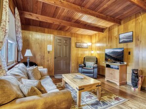 A cozy cabin interior with a wooden ceiling, a sofa, a table, a television, and a bear statue. - Bear Cub Retreat - A charming cabin less than a mile to Gatlinburg! (Gatlinburg)