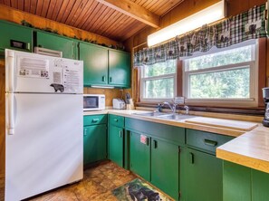 Eine Küche mit grünen Schränken, einem weißen Kühlschrank, einer Mikrowelle, einem Spülbecken und einem Fenster mit einem Karomuster-Vorhang.