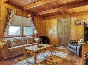 A cozy living room with a wooden ceiling, a sofa, a coffee table, a rug, and a door. - Bear Cub Retreat - A charming cabin less than a mile to Gatlinburg! (Gatlinburg)
