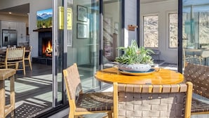 A modern outdoor dining area with a fireplace, glass doors, and a view of the mountains. - Summit Trails Retreat – Indoor Pool, Home Theater, Hot Tub | Sleeps 16!!! (Sevierville)
