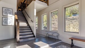 Eine Treppe mit Holzstufen und einer Holzreling, die zu einer Empfangshalle mit großen Fenstern und einer Bank führt.