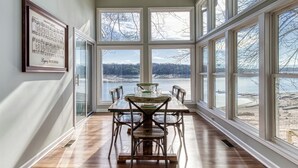 Comedor con una mesa grande, sillas y vistas a un lago a través de amplias ventanas.