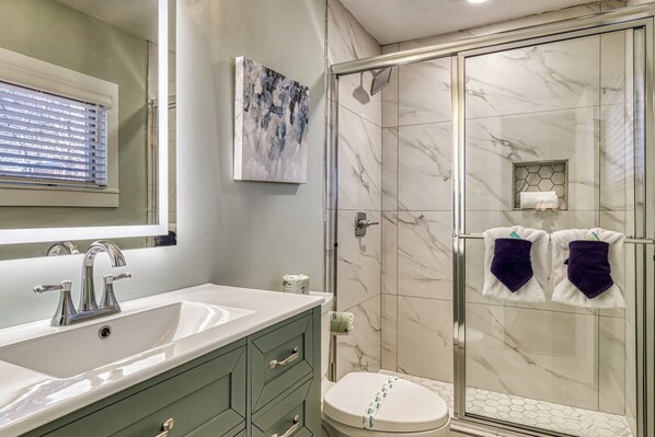 Een badkamer met een glazen douche, een wastafel met spiegel en een toilet.