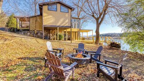 Una casa moderna con base de piedra, una amplia terraza y un brasero rodeado de sillas Adirondack.
