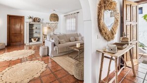 A living room with a sofa, coffee table, and decorative items. There is a door, a shelf with plants, and a mirror with a wreath. - Casa del Mar. Spectacular villa with sea views and jacuzzi in Charco del Palo (Chraco del Palo - Haría)