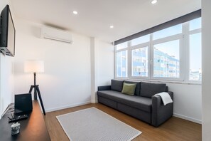 Una sala de estar moderna con un sofá, una lámpara, una computadora portátil y vistas a edificios a través de amplios ventanales.