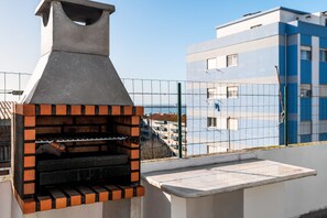 Una parrilla para barbacoa en la azotea, con vistas a un edificio azul y una valla.