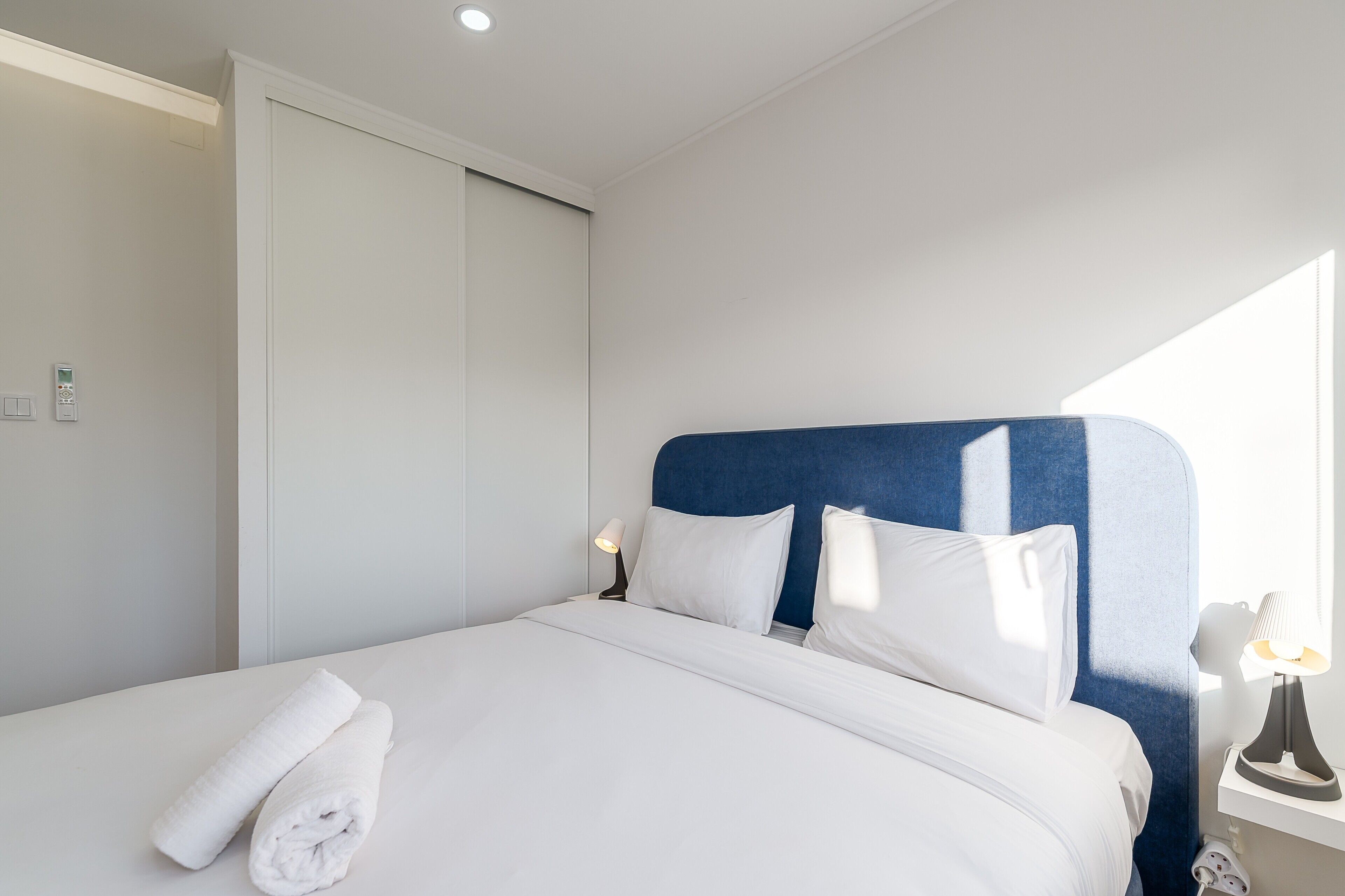 Cama bem arrumada com lençóis brancos, cabeceira azul e abajur.