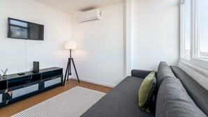 A modern living room with a flat-screen TV, a standing lamp, a sofa, and a window. - Apartment 'M J House' with Sea View, Wi-Fi and Air Conditioning (Setúbal)