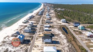 Luchtbeeld van een kustwoongebied met huizen langs het strand, een weg parallel aan de kustlijn, en een logo voor Fort Morgan Properties by Reed Real Estate.