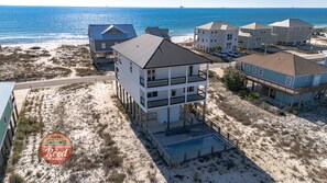 A beachfront property with multiple buildings, including a two-story house with a balcony and a swimming pool. - Coastal Comfort — Luxurious New Construction with Stunning Gulf Views (Gulf Shores)