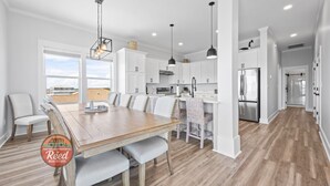 Een moderne keuken met witte kastjes, een houten eettafel en hangende lampen.