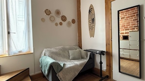 A cozy bedroom with a bed, a small table, a mirror, and a window with curtains. - "L'esprit Sable & Détente " Cosy studio between sea and port (Les Sables-d'Olonne)