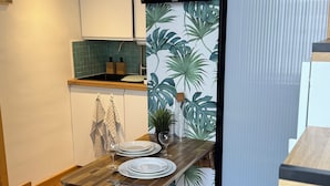 A compact kitchen with a wooden countertop, a dining table with chairs, and a sliding door with a tropical leaf pattern. - "L'esprit Sable & Détente " Cosy studio between sea and port (Les Sables-d'Olonne)