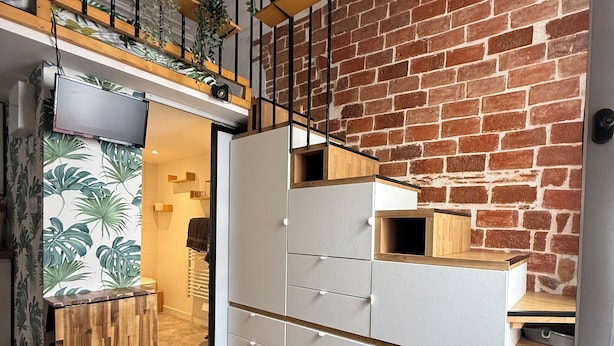 A modern living room with a brick wall, wooden flooring, a white storage unit, and a green sofa. - "L'esprit Sable & Détente " Cosy studio between sea and port (Les Sables-d'Olonne)