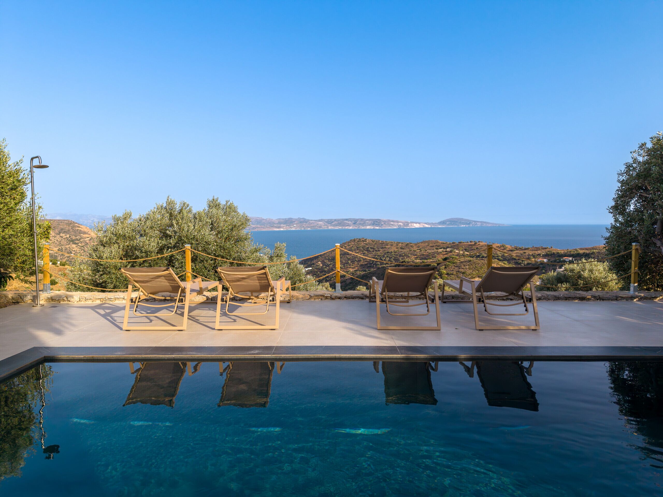 A pool with clear water, surrounded by lounge chairs and a view of the sea.