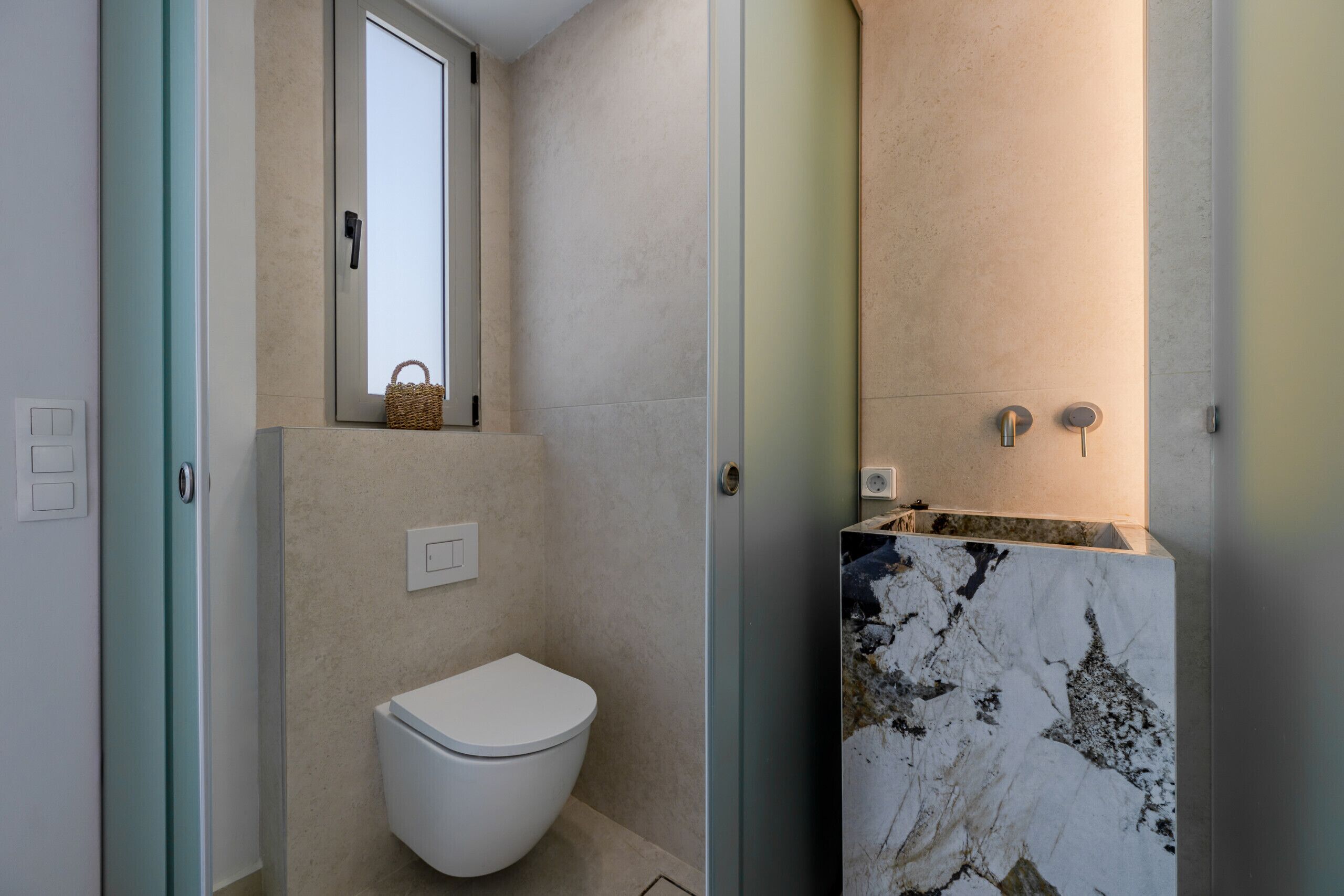 Ein Badezimmer mit Toilette, einem kleinen Fenster und einem Marmorwaschbecken.
