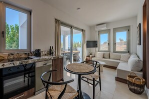 Eine moderne Küche mit Einbauofen und Geschirrspüler, ein Essbereich mit rundem Tisch und Stühlen sowie ein Wohnbereich mit Sofa und Fernseher.