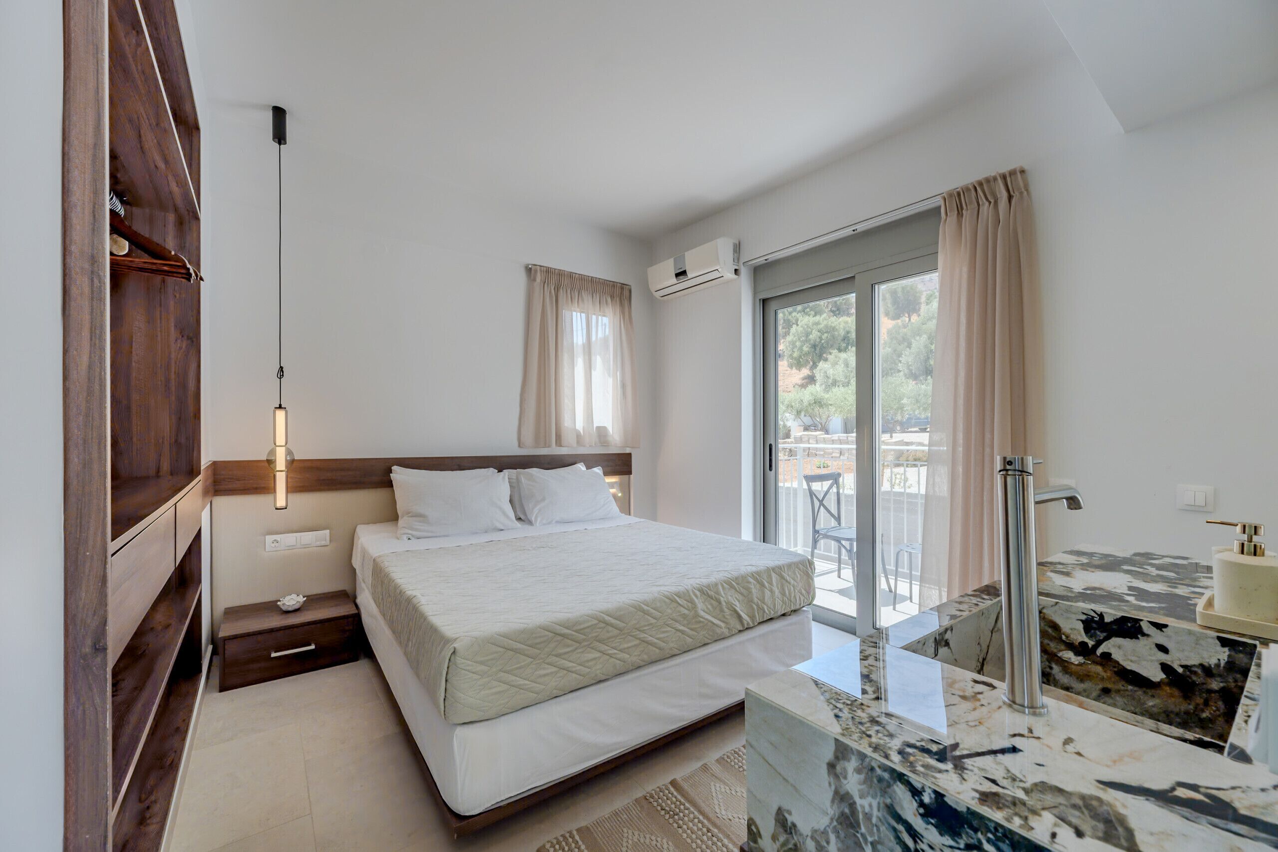 A bedroom with a bed, bedside table, and a bathroom with a sink and mirror.