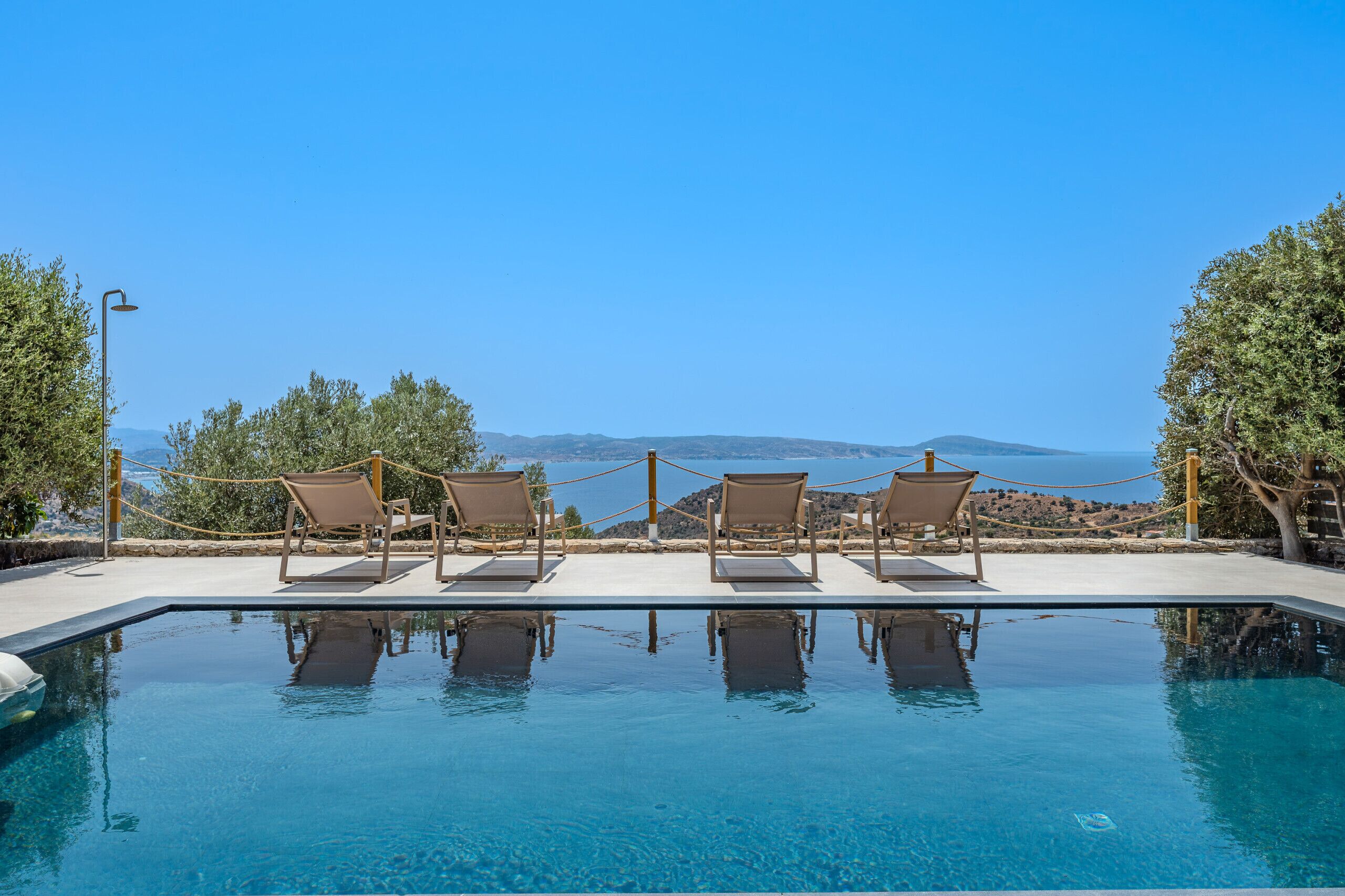 Una piscina azul cristalina con sillas de descanso y vistas al mar.