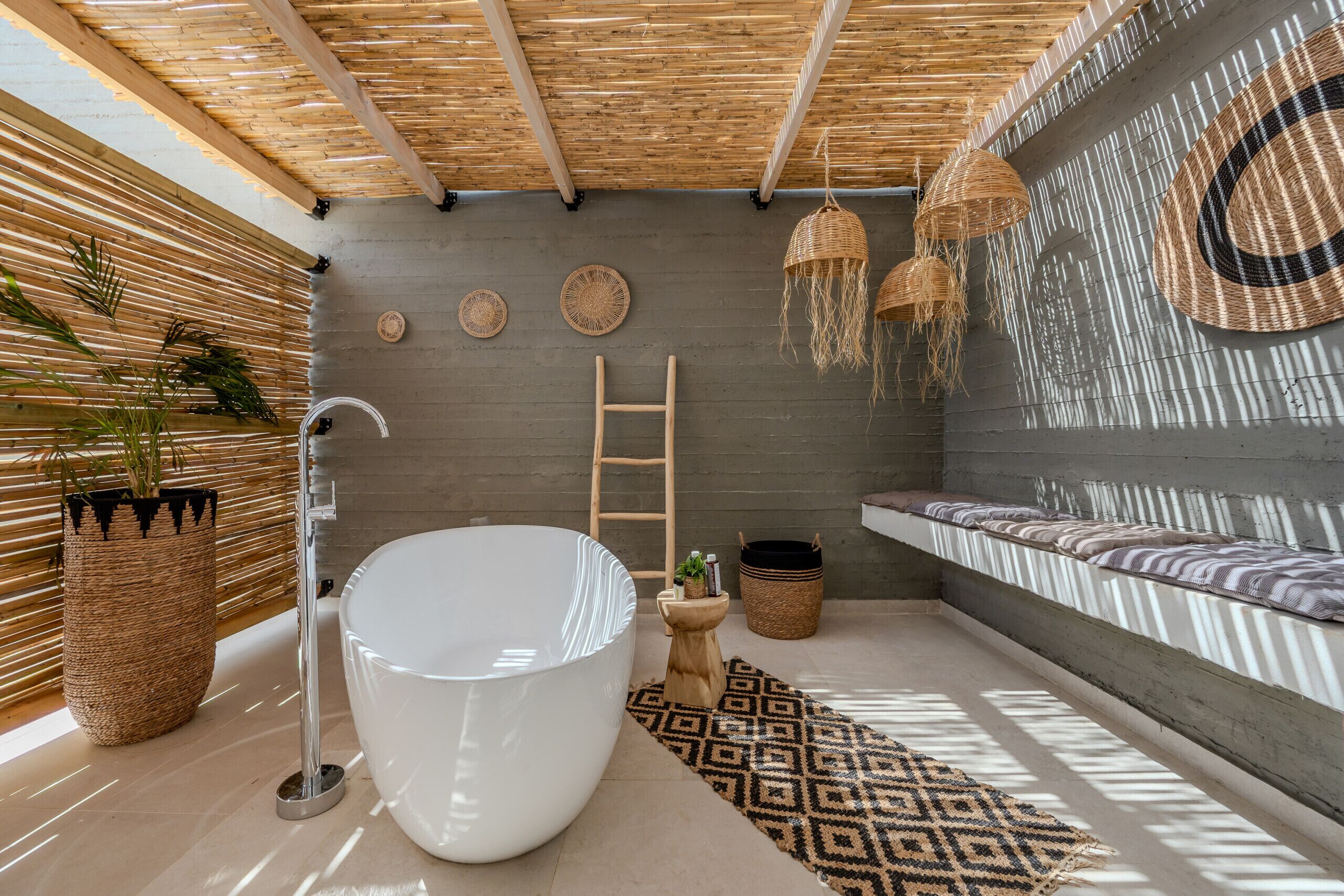 Un baño moderno con una bañera grande, techo de listones de madera y pared de concreto con un adorno de pared tejido.