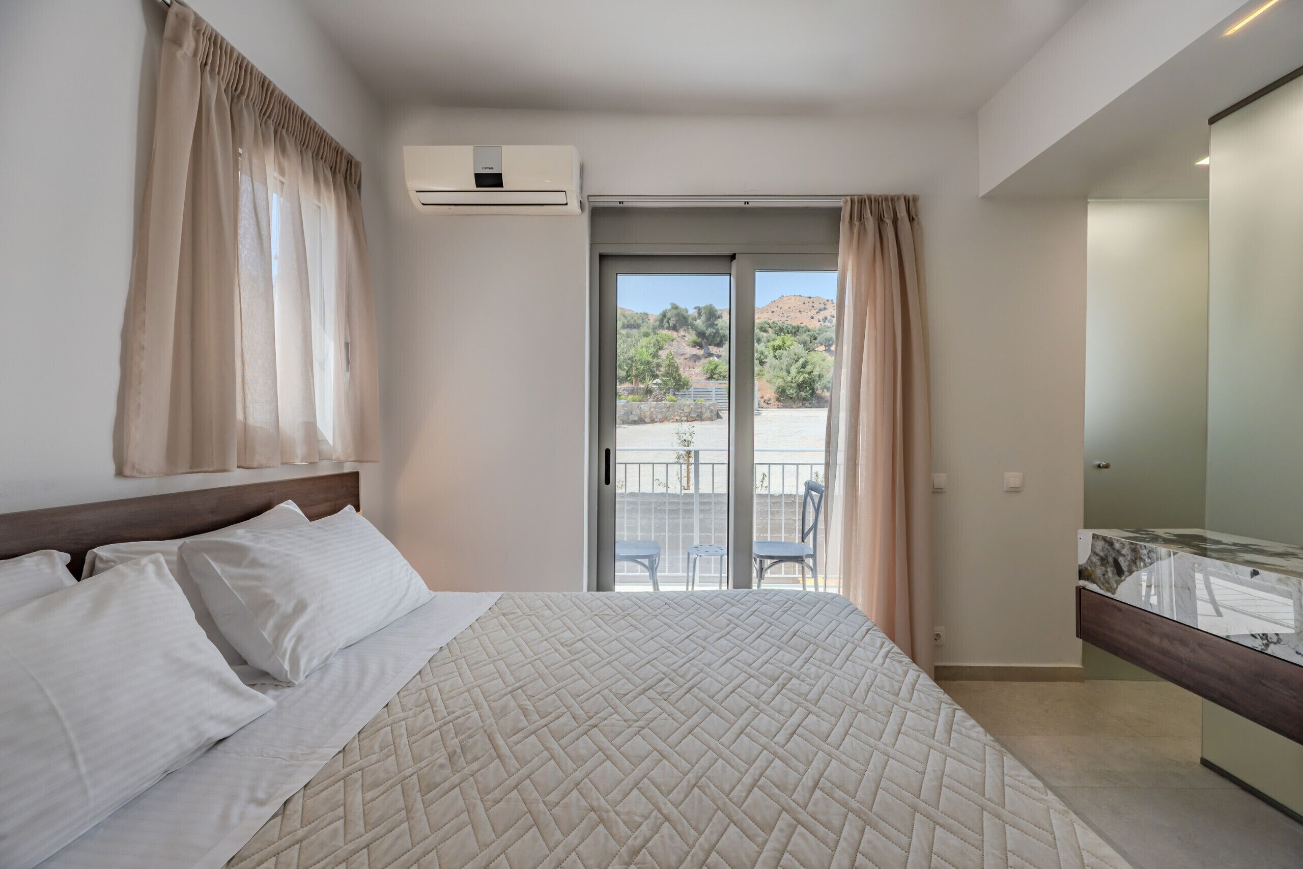 A hotel room with a bed, a balcony with a view, and an air conditioning unit.