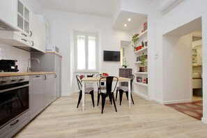 A modern kitchen with white cabinets, a wooden countertop, and a built-in oven. There is a dining table with four chairs and a flat-screen TV mounted on the wall. - Lovely two-bedroom apartment near vatican  (Roma)