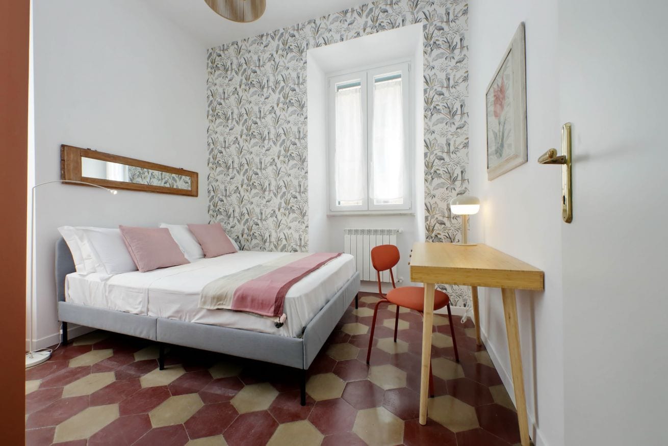 A bedroom with a bed, a desk, a chair, a window, and a radiator.