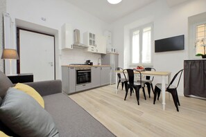 Una cucina moderna con mobili bianchi, un tavolo da pranzo con sedie e un televisore a schermo piatto montato a parete.