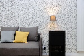 A grey sofa with two cushions, a black entertainment unit, and a wall with a floral pattern. - Lovely two-bedroom apartment near vatican  (Roma)