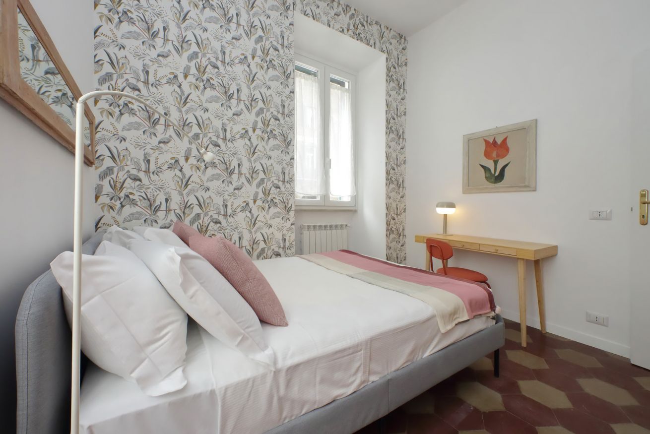 A bedroom with a bed, a desk, and a window.
