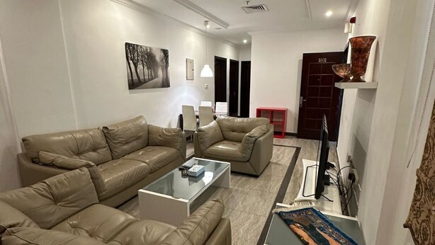 A modern living room with a sectional sofa, a coffee table, and a rug. There is a painting on the wall and a door in the background.
