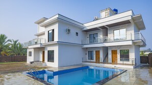 Ein modernes, zweistöckiges Haus mit Schwimmbad, Balkon und einem Wassertank auf dem Dach.