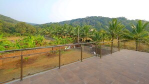 Eine Terrasse mit Blick auf eine üppige Landschaft, einschließlich Palmen und einer hügeligen Kulisse.