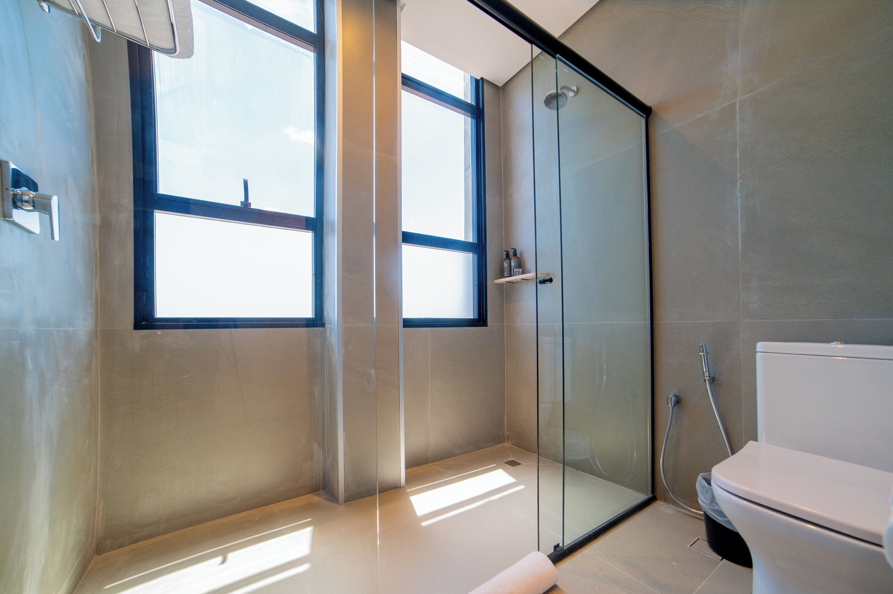 A modern bathroom with a glass shower enclosure, a toilet, and a window providing natural light.