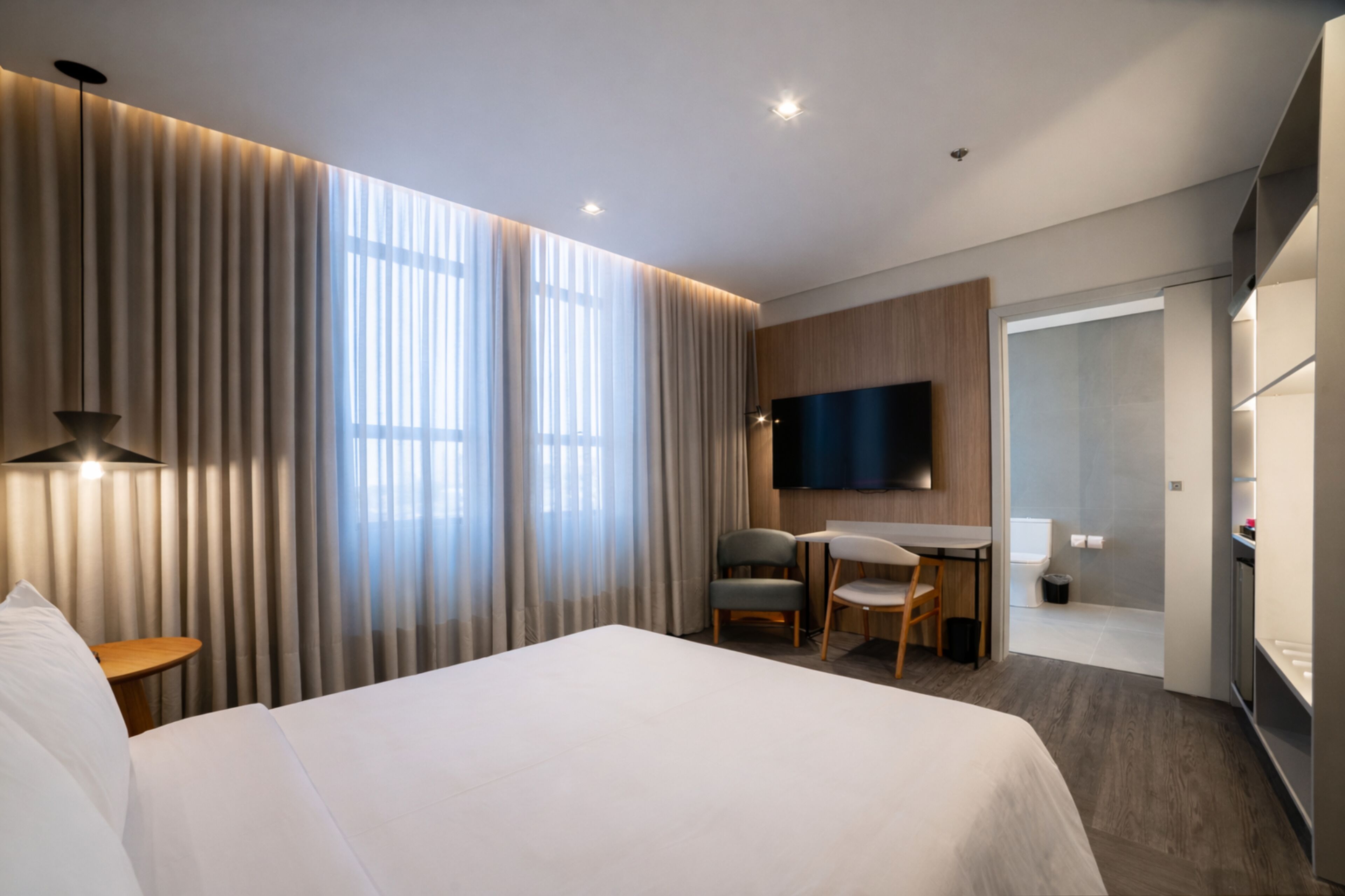 A modern hotel room with a large bed, a desk with two chairs, a flat-screen TV, and a shower area.