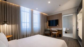A modern hotel room with a large bed, a desk with two chairs, a flat-screen TV, and a shower area.