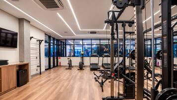A modern gym with exercise equipment, a wooden floor, and large windows.