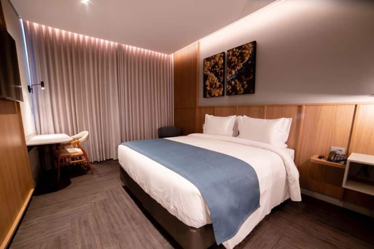A hotel room with a bed, bedside table, and a small desk with a chair.