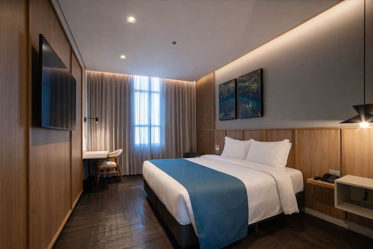 A modern hotel room with a large bed, a desk, and a TV.