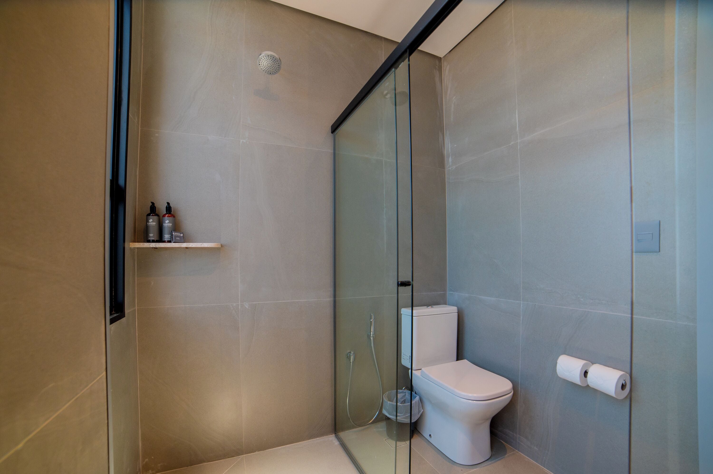 A modern bathroom with a glass shower enclosure, a toilet, and a shelf with toiletries.