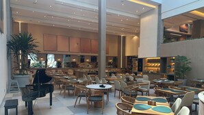 Un vaste espace intérieur aménagé avec différents types de sièges, notamment des tables et des chaises, et un piano placé à l’avant.